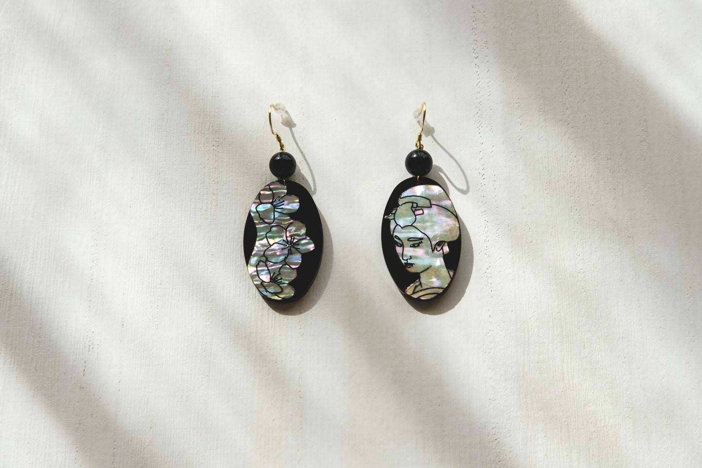 Mother of pearl earrings with engraved cherry blossms and portrait of a woman.